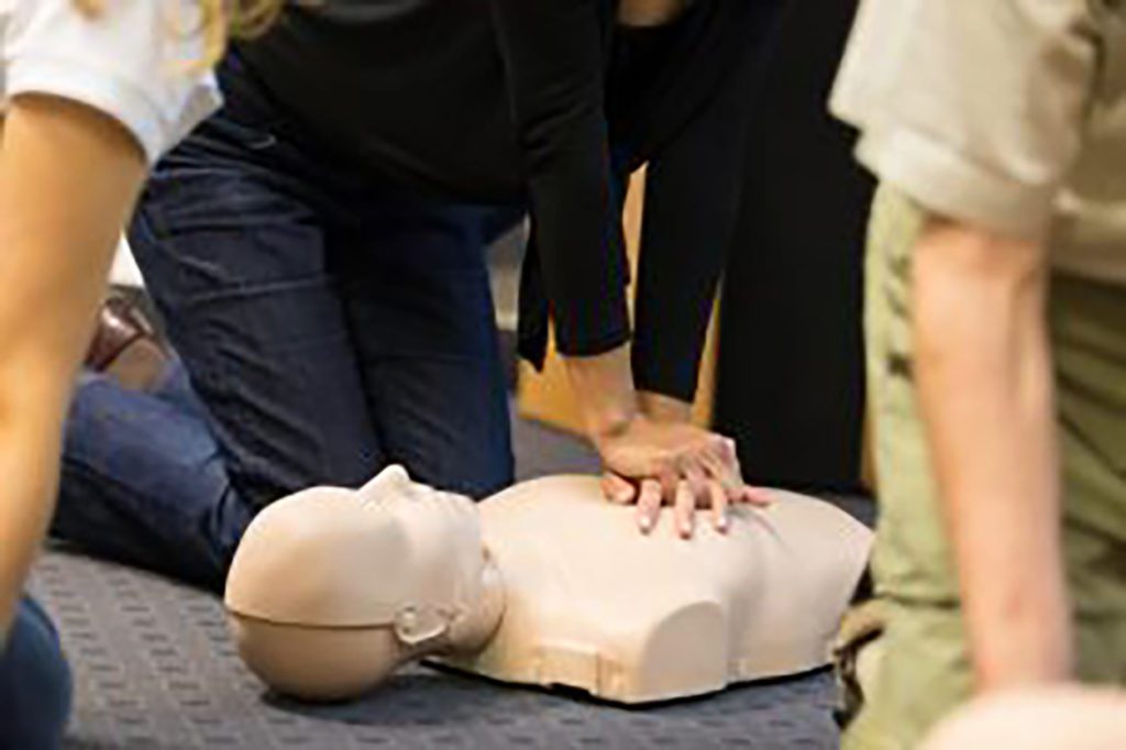 A hand of a women wearing black long sleeves practicing CPR on the dummy