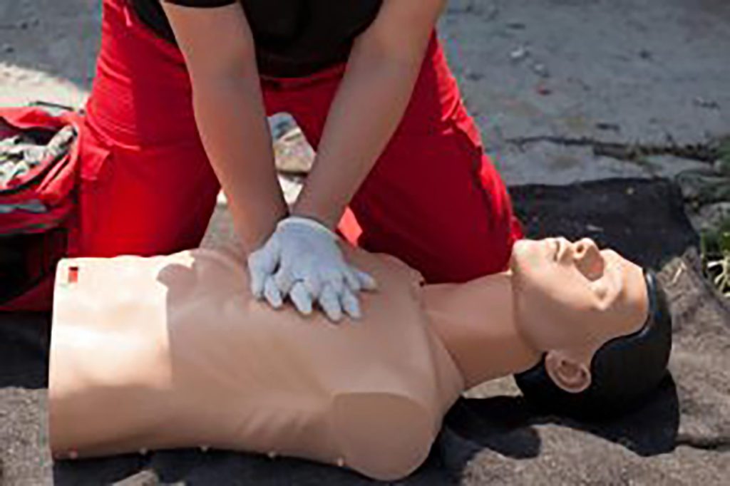 Two hands wearing white gloves having CPR on the dummy