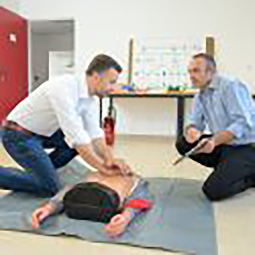 Two gentlemen practicing cpr on the dummy inside the office